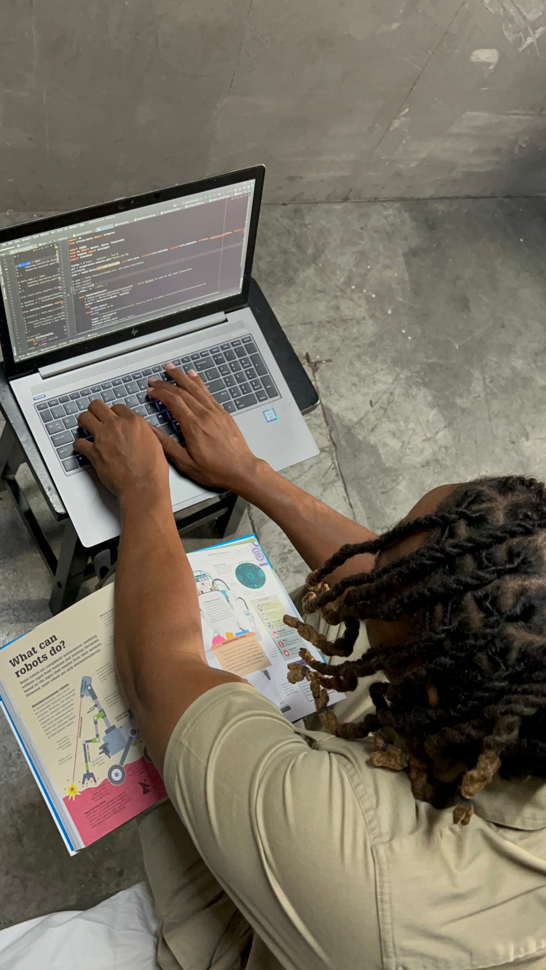 Antoine self-teaching to code, robotics magazine open beside the laptop